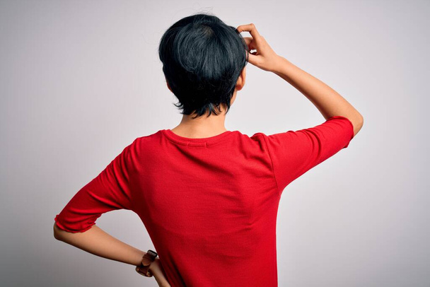 Młoda piękna azjatycka dziewczyna w luźnej czerwonej koszulce stojącej nad odizolowanym białym tłem do tyłu myśląc o wątpliwościach z ręką na głowie - Zdjęcie, obraz