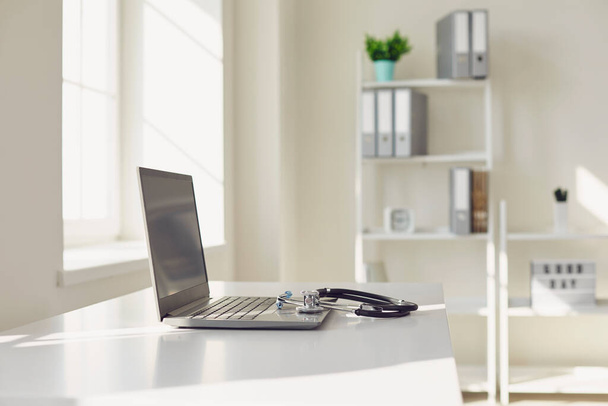 Doctor online. A stethoscope is on a white table with a laptop in blur at the hospital office. - Foto, imagen