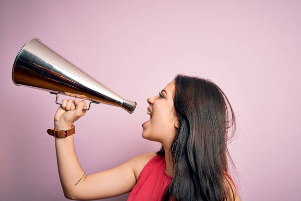 Молода красива брюнетка спікер жінка кричить спілкуватися, використовуючи старовинний мегафон, що стоїть над ізольованим рожевим тлом
 - Фото, зображення