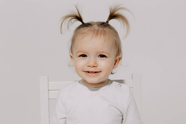 cute little girl with a ponytail hairstyle dressed in a white T-shirt and denim pants posing for a photo on a white background in a photo studio - Фото, изображение