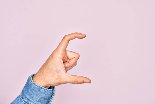 Hand eines kaukasischen jungen Mannes mit Fingern über isoliertem rosa Hintergrund, der unsichtbares Ding nimmt und Objekt mit Fingern hält, die Raum zeigen - Foto, Bild