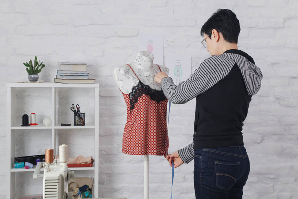Kleermaker past kledingontwerp aan op etalagepop in werkplaats - modeatelier, slow fashion, tailor craft, handgemaakte kleding - Foto, afbeelding