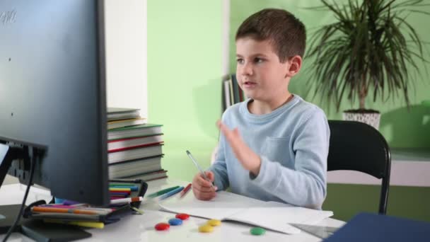 home schooling, handsome smart boy teaches home lessons sitting at a computer and watching a video lesson on a monitor screen - Πλάνα, βίντεο