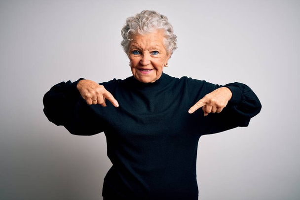 Seniors belle femme portant casual pull noir debout sur fond blanc isolé regardant confiant avec sourire sur le visage, se pointant avec les doigts fiers et heureux
. - Photo, image