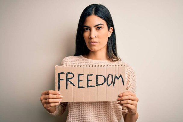 Young beautiful hispanic woman holding protest banner of freedom asking for liberty with a confident expression on smart face thinking serious - Photo, image