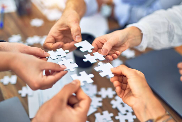 Werknemers met handen aan elkaar die puzzelstukjes op kantoor met elkaar verbinden - Foto, afbeelding