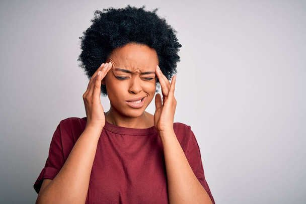Junge schöne afroamerikanische Afro-Frau mit lockigem Haar in lässigem T-Shirt, die mit der Hand auf dem Kopf vor Schmerzen im Kopf wegen Stress steht. Migräne. - Foto, Bild