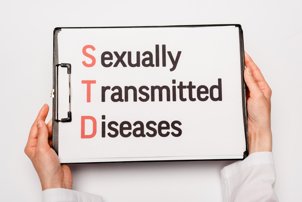 καλλιεργημένη άποψη του γιατρού κρατώντας πρόχειρο με σεξουαλικά μεταδιδόμενα νοσήματα γράμματα απομονώνονται σε λευκό  - Φωτογραφία, εικόνα