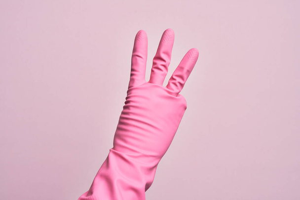 Hand of caucasian young man with cleaning glove over isolated pink background counting number 3 showing three fingers - Fotoğraf, Görsel