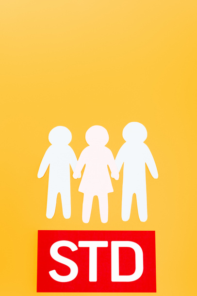 Kırmızı kağıdın yanında, turuncu üzerine STD harfleri izole edilmiş üç kağıttan insan var. - Fotoğraf, Görsel