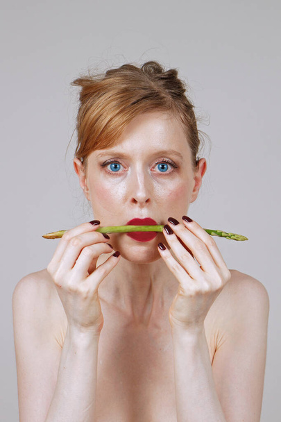 Young woman holding raw asparagus between her red lips - 写真・画像