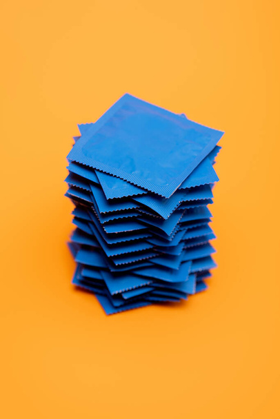 stacked condoms in blue packs isolated on orange  - Фото, изображение