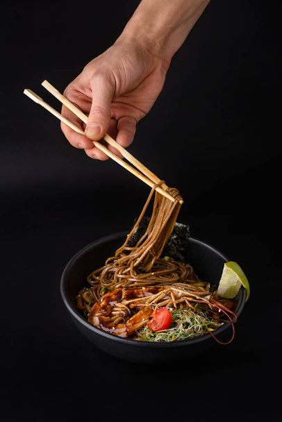 Asiatisches Gericht Buchweizennudeln Soba mit Gemüse, Huhn und Garnelen und zwei Essstäbchen auf dunklem Hintergrund - Foto, Bild