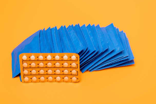 fogamzásgátló tablettát tartalmazó buborékcsomagolás narancssárga színű óvszert tartalmazó csomagolás közelében  - Fotó, kép