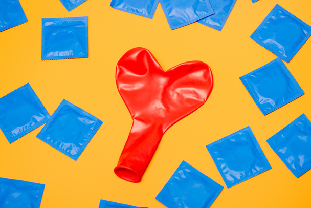 top view of red heart-shaped balloon near blue condoms isolated on orange  - Foto, Bild