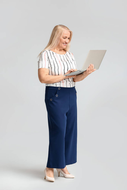 Portrait of mature businesswoman with laptop on light background - Foto, imagen