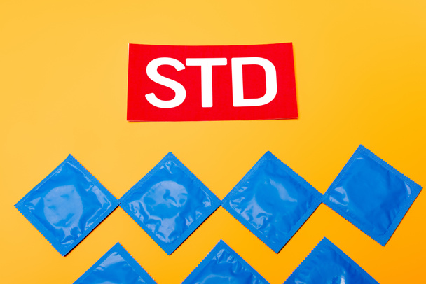 bovenaanzicht van verpakkingen met condooms in de buurt van rode STD letters geïsoleerd op oranje  - Foto, afbeelding