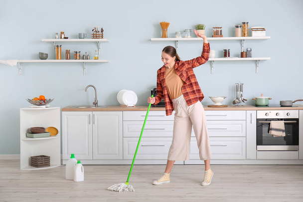 Jeune femme s'amuser tout en nettoyant le sol dans la cuisine
 - Photo, image