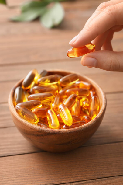Woman taking fish oil capsule from bowl on table - Photo, Image
