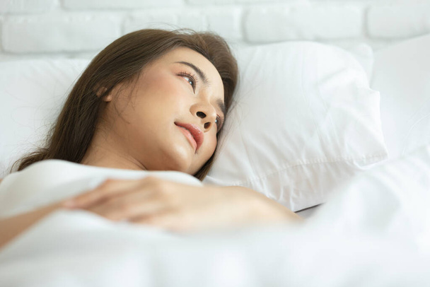 Femme asiatique gaie et en bonne santé et portant un pyjama blanc se réveiller sur le lit dans la chambre le matin.à la maison en vacances
. - Photo, image