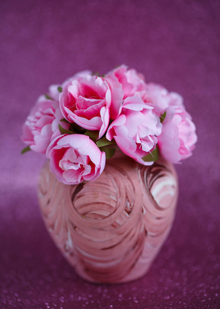 Mooie kleine roze bloemen in een kleine vaas met een patroon op een donkerroze glanzende achtergrond - Foto, afbeelding
