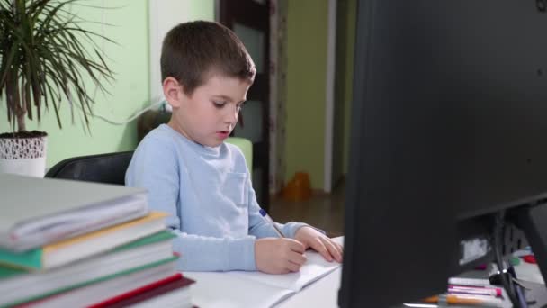 smart elementary school student learns lessons at home sitting at computer and watches video broadcast of lesson with teacher on monitor screen - Footage, Video