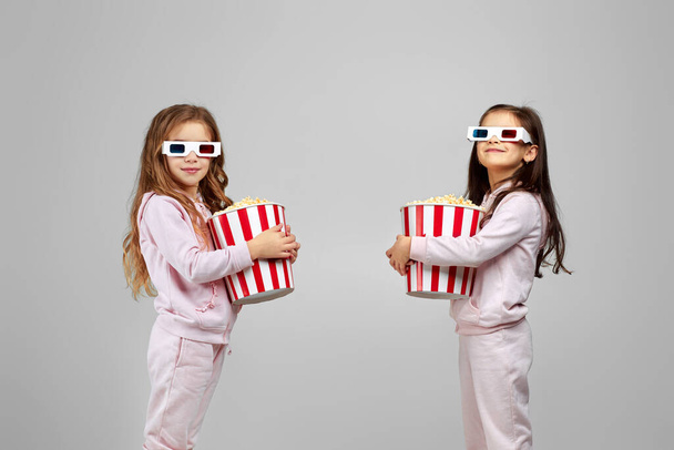 two little girls in red-blue 3d glasses holding popcorn buckets - 写真・画像