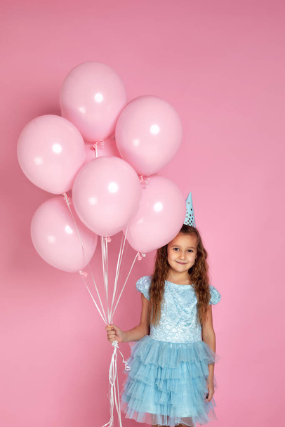 little child girl in dress and birthday hat celebrating with pastel pink air balloons - Фото, изображение