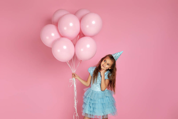 little child girl in dress and birthday hat celebrating with pastel pink air balloons - Photo, Image