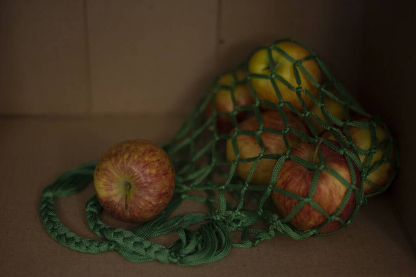 Натюрморт з яблуками: яблука в зеленій сітці на тлі картонної коробки
 - Фото, зображення