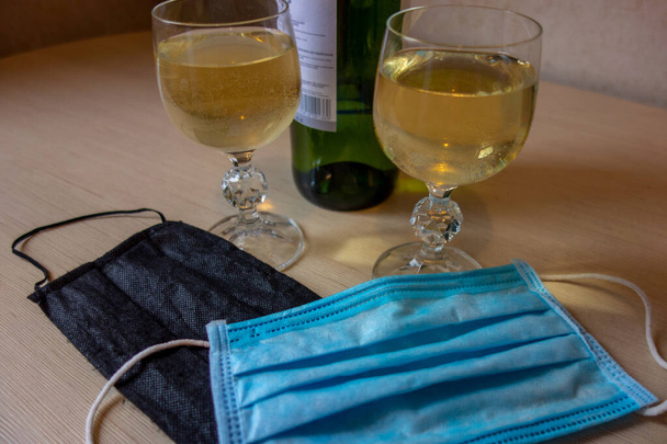Ρομαντικό ραντεβού σε πανδημικό κόσμο. Δύο ποτήρια και ένα μπουκάλι κρασί με δύο ιατρικές μάσκες στο τραπέζι. Έννοια των νέων χρόνων και αλλαγή του τρόπου ζωής λόγω καραντίνας κλειδώματος  - Φωτογραφία, εικόνα