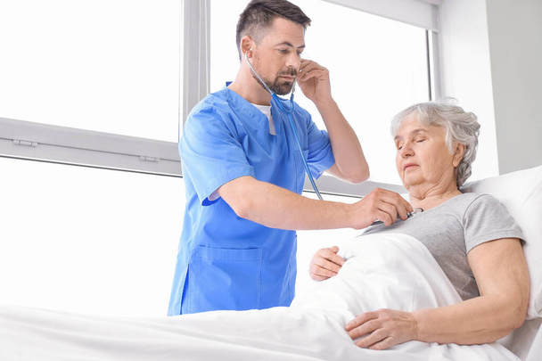 Mieslääkäri, joka työskentelee iäkkään potilaan kanssa sairaalahuoneessa
 - Valokuva, kuva
