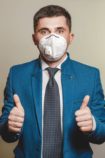 Erős férfi, üzletember nyakkendőben és orvosi maszkban bizonyítja a bizalmat a munkában a pandémiás koronavírusban. Mindkét kéz hüvelykujját mutatja 2021-ben. - Fotó, kép