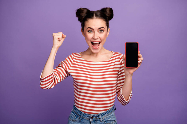 Photo of funny crazy lady hold new model smart phone touch screen raise fist win free lottery smart phone sale wear white red casual striped shirt isolated purple pastel color background - Zdjęcie, obraz