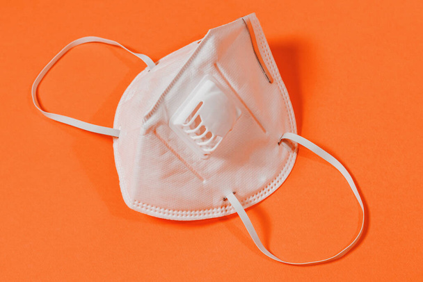 Ιατρική μάσκα με βαλβίδα και χειρουργική μάσκα σε πορτοκαλί φόντο 2021 - Φωτογραφία, εικόνα