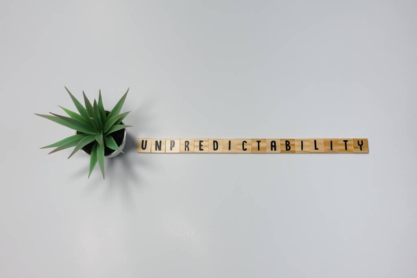 Het woord Onvoorspelbaarheid geschreven in houten lettertegels op een witte achtergrond. Concept onvoorspelbaarheid in het bedrijfsleven, reizen en mensen. - Foto, afbeelding