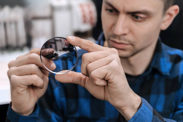 Young professional optician is working with lens in optical workshop using special tools and equipment. Master measuring len, repairing and fixing eye glasses - Фото, изображение
