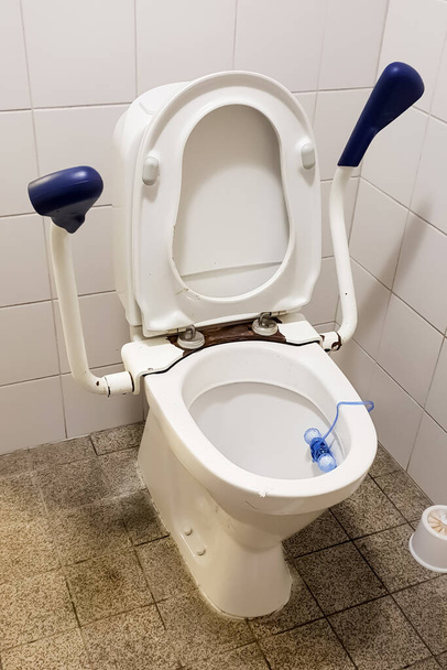 Κοντινό πλάνο βρώμικης δημόσιας τουαλέτας για άτομα με αναπηρία και ηλικιωμένους με χειρολισθήρες στο καμαρίνι ή στο νοσοκομείο ή σε δημόσιο χώρο. - Φωτογραφία, εικόνα