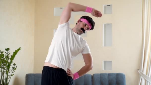 Funny athletic man in the home gym doing a stretch spreading his arms - Materiał filmowy, wideo