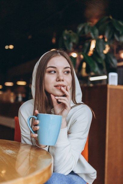 07.03.2020 Odessa, Ukraine: attractive young girl drinking coffee in a cozy cafe, beginning of spring, she smiles and enjoys life - Foto, Imagem