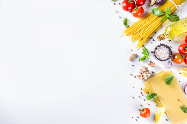 Italiaanse voedselingrediënten voor het koken van spaghetti pasta. Rauwe spaghetti pasta met verschillende ingrediënten - ui, tomaten, knoflook, basilicum, peterselie, kaas, olijfolie. Op witte tafel achtergrond, platte kopieerruimte - Foto, afbeelding