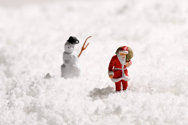 Miniatur-Weihnachtsmann und ein Schneemann im frischen Winterschnee in einer traditionellen Weihnachtsszene, um die Weihnachtszeit mit Kopierraum für Ihren Gruß zu feiern - Foto, Bild
