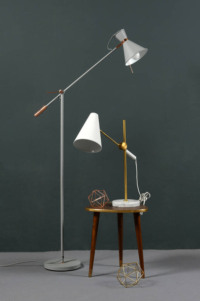 Két évjáratú szöglámpa, egy szabadon álló padlólámpa, és egy asztali lámpa egy széken, egy szürke falnak támasztva beltérben. - Fotó, kép