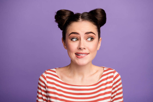 Oops I did it again. Closeup photo of pretty funny lady two cute buns look side empty space biting lips wear white red casual striped shirt isolated purple pastel color background - Foto, Imagen