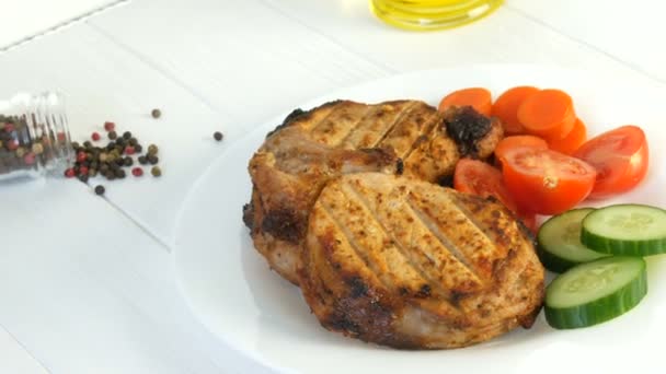 Вкусные сочные свежие ломтики жареного стейка вокруг свинины рядом с помидорами черри и свежими овощами огурцы на белой тарелке ресторана
 - Кадры, видео