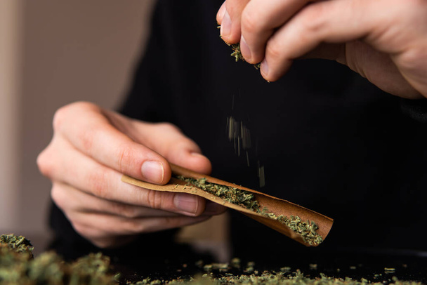 Close up marijuana joint with lighter. Man rolling a marijuana weed blunt. Man rolling marijuana cannabis blunt. - Фото, изображение