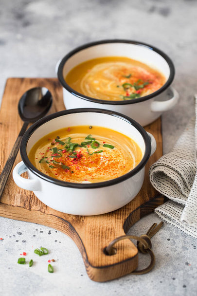 Pumpkin cream soup. Roasted pumpkin and carrot puree soup with turmeric, cream, paprica, chives and pumpkin seeds on grey background. Vegetarian cousine. Vegan recipe. Green living. Organic food. - Photo, Image