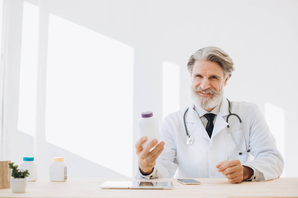 Portrait of a senior doctor holding a bottle of medication in a hospital - Zdjęcie, obraz
