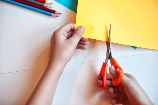 Das Kind schneidet die Anwendung von Buntstiften auf einem Hintergrund aus weißem und farbigem Papier aus. Buntstift auf weißem Hintergrund. Kinder verwenden diese Bleistifte als häusliche Aktivitäten und Anwendungen. - Foto, Bild