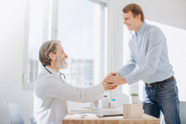 Senior doctor shaking hands with patient while meeting at doctor's office. - 写真・画像
